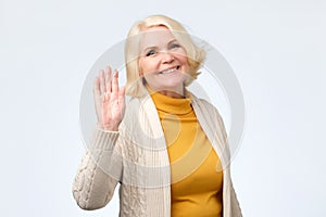 Senior woman waving her hand saying hello to her friend.