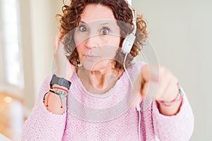 Senior woman wearing headphones listening to music pointing with finger to the camera and to you, hand sign, positive and