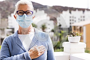 A senior woman wearing medical mask greets with hand over the heart. The new greeting recommended by the OMS World Health