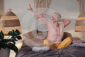Senior woman wearing pyjama smiling in bright living room stretching waking up