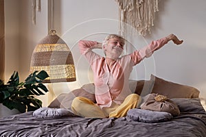 Senior woman wearing pyjama smiling in bright living room stretching waking up