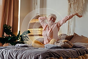 Senior woman wearing pyjama smiling in bright living room stretching waking up