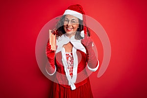 Senior woman wearing Santa Claus costume holding christmas gift over isolated red background surprised with an idea or question