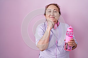 Senior woman wearing sportswear and headphones with hand on chin thinking about question, pensive expression