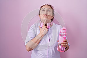 Senior woman wearing sportswear and headphones thinking concentrated about doubt with finger on chin and looking up wondering