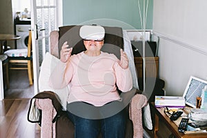 Senior woman wearing virtual reality goggles at home. Emotional lady with virtual headset or 3d glasses playing video