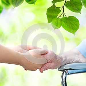 Senior woman in wheel chair holding hands with young caretaker photo
