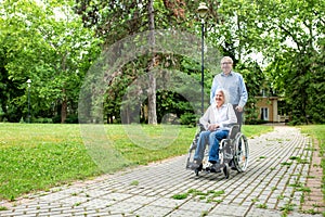 Senior woman in wheelchair being pushed through the park by her man