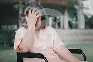 A senior woman in wheelchair who has a severe headache suffers from a stroke, brain disease, patient holding head with hand,