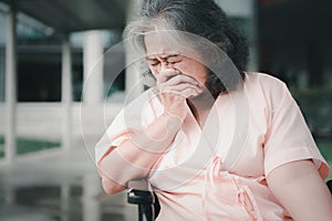 A senior woman in wheelchair who has a severe headache suffers from a stroke, brain disease, patient holding head with hand,