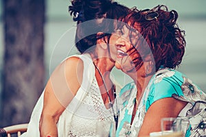 Senior woman whispering something to her friends ear in a cafe