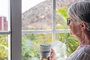 Senior woman at the window holding a coffee cup looking out