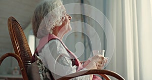 Senior woman, window and thinking with tea in home for vision, memory and relax in rocking chair. Elderly person, coffee