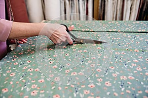 senior woman working in atelier shop with rolls of fabrics. Cutting fabrics. Small business