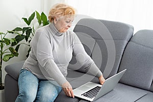 Senior woman is working on her laptop computer sitting on a sofa at home