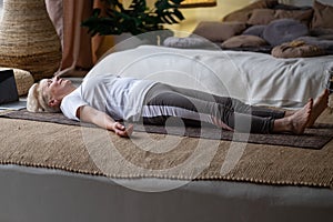 Senior woman working out at home, doing yoga exercise lying in Shavasana or Corpse or Dead Body Posture photo