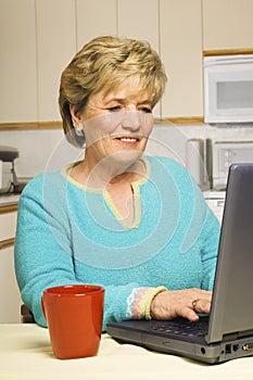 Senior woman works on her laptop in her kitchen