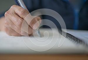 Senior woman wrinkle hand holds pen handwriting diary, letter or the will on a notebook.