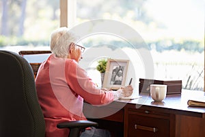 Senior Woman Writing Memoirs In Book At Desk photo