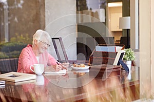 Senior Woman Writing Memoirs In Book At Desk