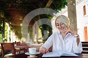Senior woman writing to notebook or diary at a cafe
