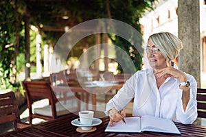 Senior woman writing to notebook or diary at a cafe