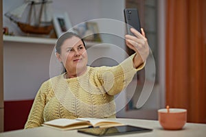 Senior woman in yellow sweater taking selfie with smart phone