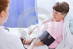 Senior woman with blood pressure monitor on her arm and young intern at hospital