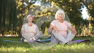 Senior women doing breezing exercises sitting in lotus position in park, energy photo
