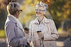 Senior women or friends drinking coffee walking along park