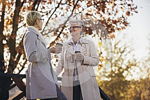 Senior women or friends drinking coffee walking along park