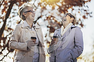 Senior women or friends drinking coffee walking along park