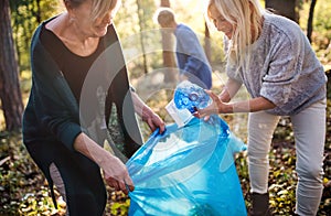 Senior women friends picking up litter outdoors in forest, a plogging concept.