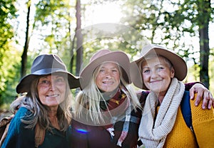 Senior women friends walking outdoors in forest, looking at camera.