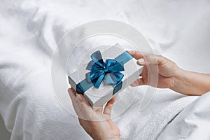 Senior women hands holding gift box with blue ribbon and Sleep on the bed with a white blanket