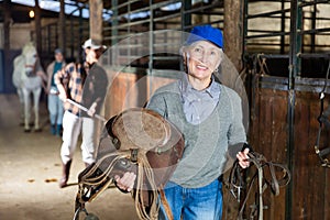 Senior woman horse breeder with leather saddle and tack