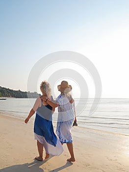 Senior women walking barefoot at beach line at sunset. Vertical photo