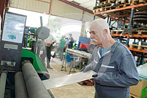 Senior worker handling sheet metal plates onto machinery