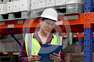 Senior worker man wearing safety vest and helmet, holding file folder document at cargo logistic warehouse. Asian staff man