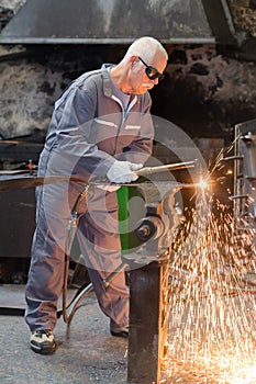 Senior worker in protective mask welding steel railings outdoors