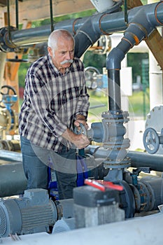 Senior worker turns bypass valve on gas compressor station