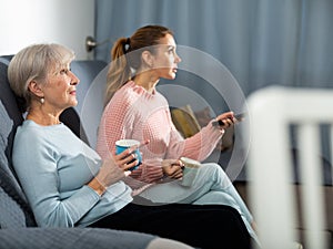 Senior and younger women watching TV and drinking tea