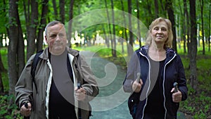 Seniors is engaged in Nordic walking in the forest. A man and a woman walk with sticks to improve health.