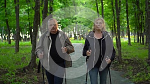 Seniors is engaged in Nordic walking in the forest. A man and a woman walk with sticks to improve health. Slow motion.