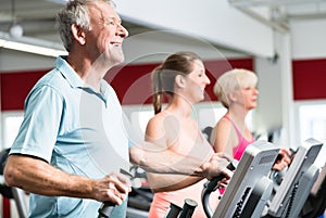 Seniors train on cross trainer with personal trainer at the gym