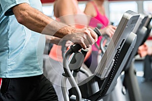 Seniors train on cross trainer with personal trainer at the gym