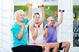 Seniors with trainer in gym at sport lifting barbell
