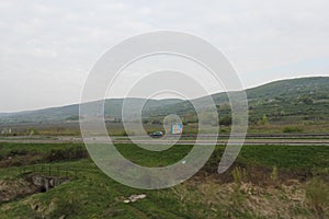 Senkvice, Slovakia - April, 2011: car moves along road near grape garden, green fields and hills view from railway carriage.
