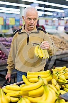 Senor man pensioner buying banana in grocery in supermarket