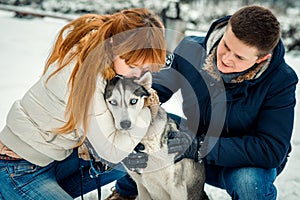 Sensitive close-up portrait of the red head woman kissing lovely siberian husky while man is stroking him. Winter time.